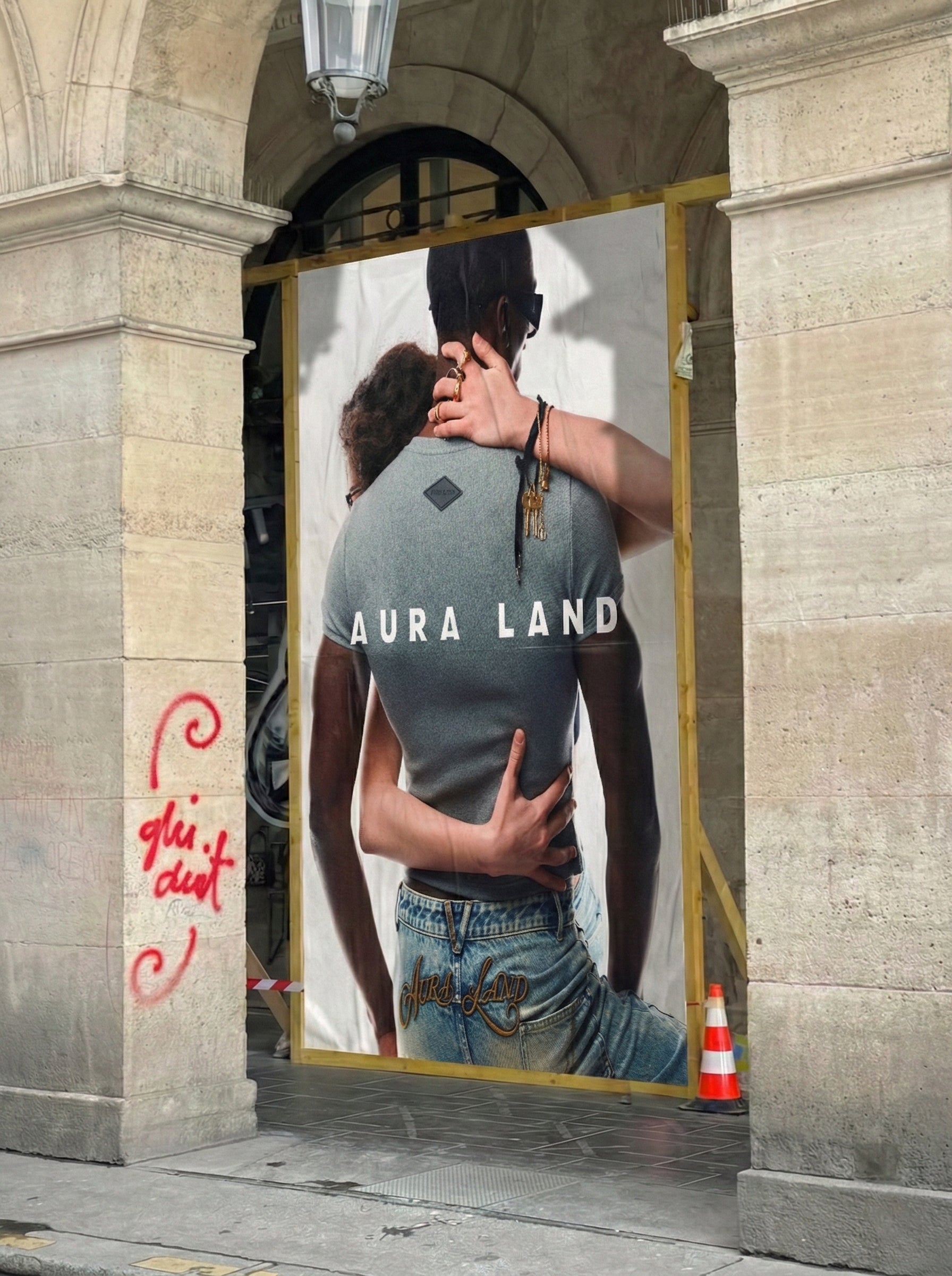 An AURA LAND poster of an embracing couple within a stone architectural archway